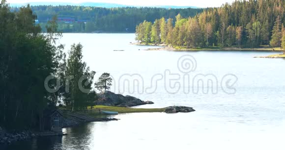 瑞典美丽的小瑞典木制木屋在岩石岛海岸在夏天阳光明媚的晚上湖泊或河流视频的预览图