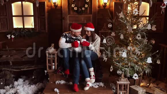 戴着圣诞帽的男朋友和女朋友坐在圣诞树旁的门廊上视频的预览图