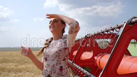 美丽的女强人喝水在收割机附近的麦田里眺望远方的谷物视频的预览图