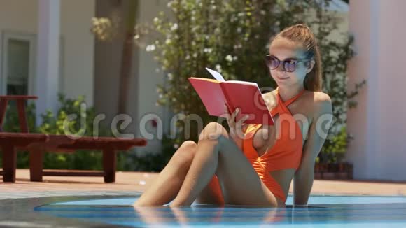 度假酒店游泳池里的金发女士阅读书籍视频的预览图