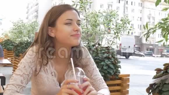年轻漂亮的黑发女人在街头咖啡馆的餐桌旁喝着夏日鸡尾酒她很高兴视频的预览图