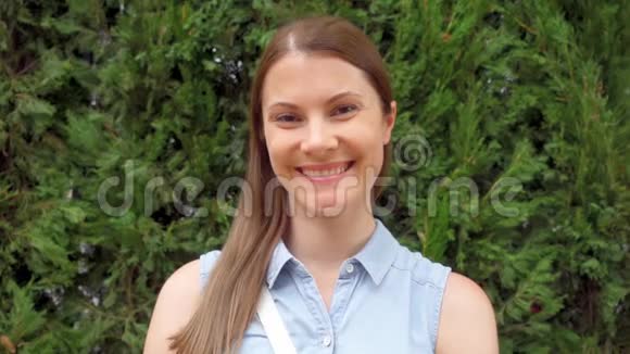 站在绿色公园的幸福微笑的年轻女人的肖像微风吹动女性的头发视频的预览图