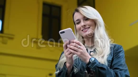 女士和使用智能手机户外漂亮的时髦女郎学生女孩在黄色手机上发短信和使用应用程序视频的预览图