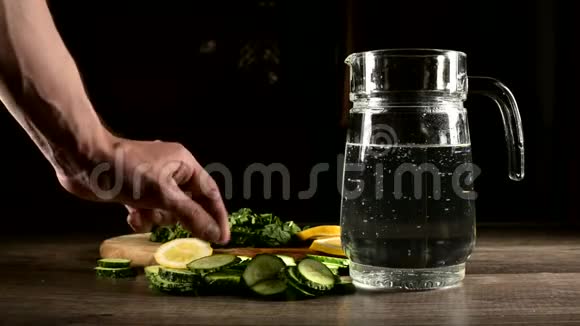 将柠檬黄瓜和薄荷叶切成薄片放在木切割板上旁边是一个带有起泡水的玻璃杯男性视频的预览图