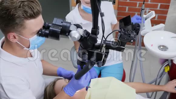 牙科医生在病人口腔内通过光学显微镜观察助手帮助附近的医院视频的预览图