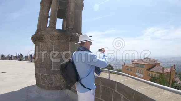 巴塞罗那的圣心寺附近一个戴着围巾和帽子的年轻人用智能手机拍摄了一段视频视频的预览图