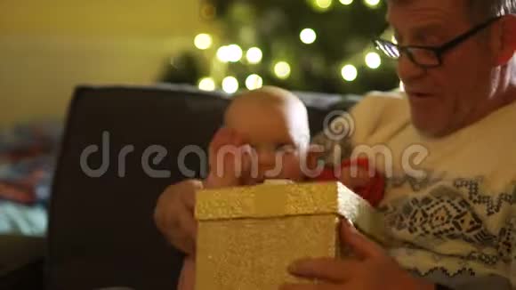 爷爷和孙子拿着圣诞礼物打开盒子在新的生日前夕他祖父的膝上视频的预览图