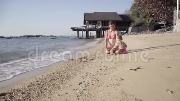母亲和女儿穿着粉红色泳衣在海边的沙滩上玩耍幸福家庭的概念4k视频的预览图