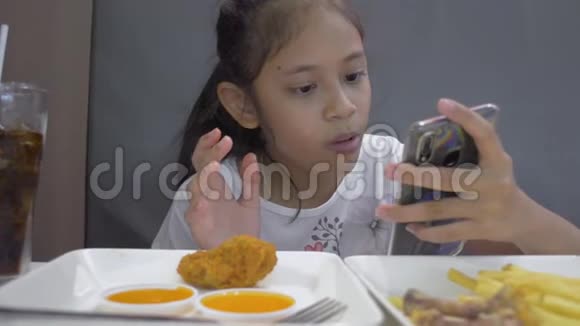 亚洲可爱的女孩吃食物而使用手机在午餐视频的预览图
