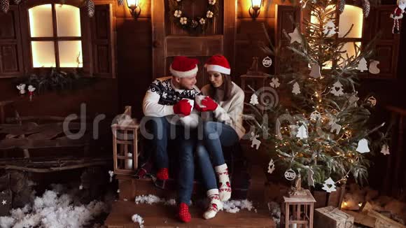 戴着圣诞帽的男朋友和女朋友坐在圣诞树旁的门廊上视频的预览图