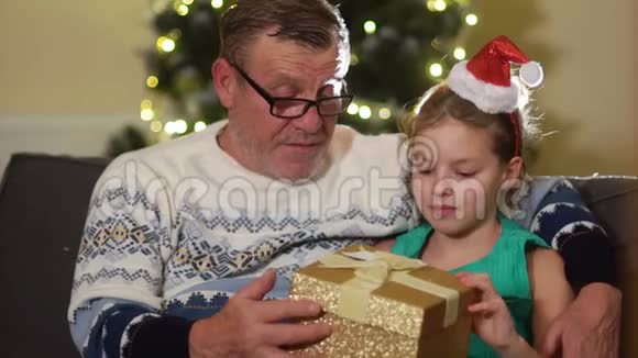 一个戴着圣诞帽的女孩抱着她的祖父感谢他的礼物家庭平安夜视频的预览图