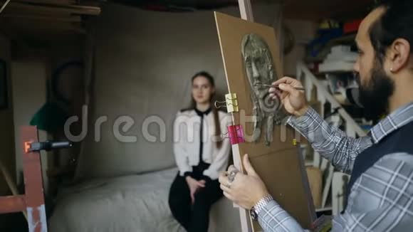 雕塑家在画室中年轻女子摆着他的姿势在画布上创作的面部雕塑视频的预览图