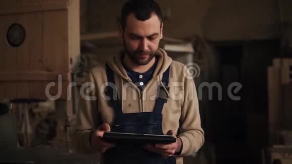 年轻的木匠手里拿着平板电脑穿过车间有木材和设备材料的车间视频的预览图