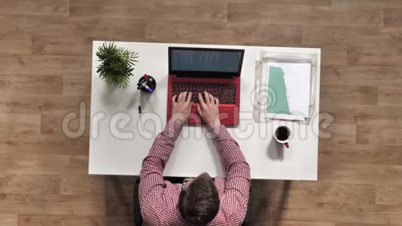 办公室职员坐在办公桌前用红色笔记本电脑打字咖啡杯笔植物图形条形图视频的预览图