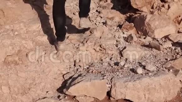 男人的腿在大沙漠石头上行走慢动作人类爬上沙漠岩石山后景又累又累视频的预览图