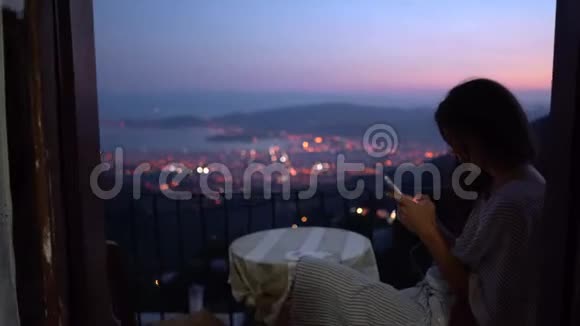 晚上女人坐在阳台上在家里使用智能手机视频的预览图