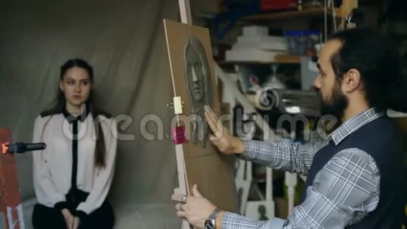 雕塑家在画室里给摆姿势的年轻女子在画布上创作人的面部雕塑视频的预览图