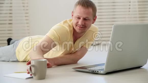快乐的男人在家里的地板上喝咖啡在笔记本电脑上聊天视频的预览图
