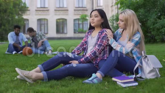 金发女孩支持她最好的朋友学生们坐在校园附近的草坪上视频的预览图