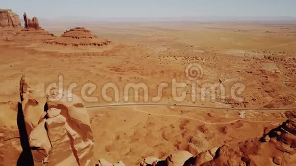 无人机靠近亚利桑那州古迹谷的高大悬崖山脉汽车沿着野生干燥的沙漠公路行驶视频的预览图