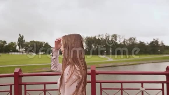 年轻漂亮的女孩走在桥上穿过公园里的湖她唱这首歌视频的预览图