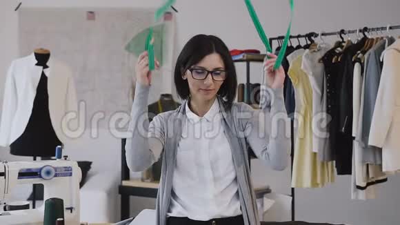 一位年轻妇女在工作时戴着眼镜和看着相机的肖像时装设计师和裁缝的特写视频的预览图