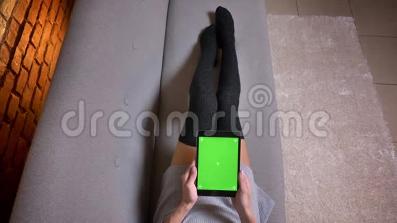 室内沙发上穿着可爱袜子的女腿特写镜头女性拿着绿色屏幕的平板电脑视频的预览图