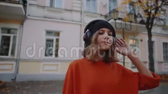 可爱的年轻女孩走在建筑物之间听音乐耳机城市风格时尚时髦的青少年视频的预览图