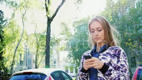 迷人的女人在城里散步喜欢智能手机太阳光芒落下美丽的高光视频的预览图