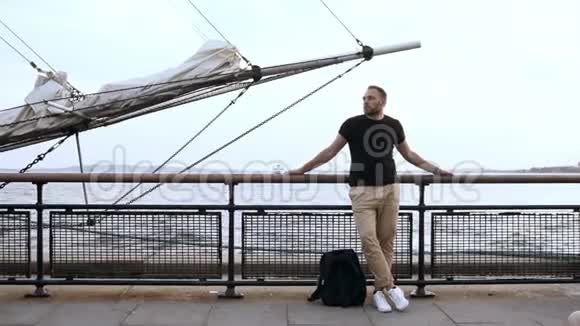 英俊的年轻人站在码头上靠近船首的栅栏环顾四周视频的预览图