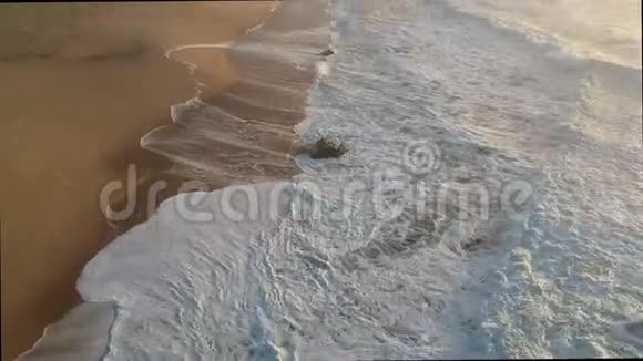 日出时在波涛汹涌的白浪上缓缓降落在海滩上视频的预览图