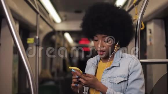 非洲裔美国年轻女性戴着耳机听音乐和在公共场合浏览手机的肖像视频的预览图