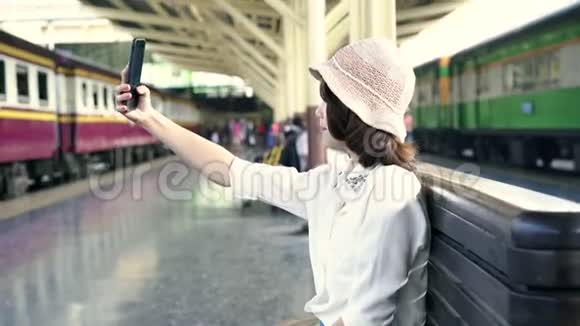快乐亚洲女乘客与休闲自拍智能手机在火车站轨道旅行曼谷市视频的预览图
