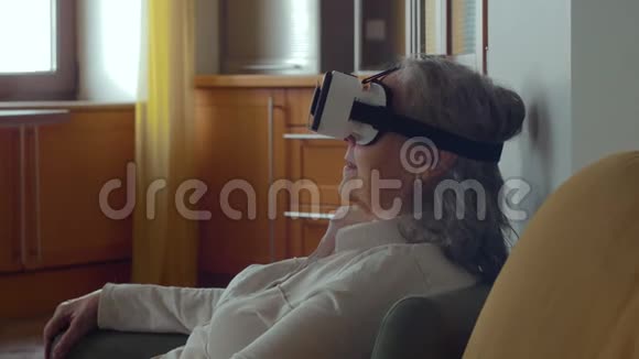 老年女性坐在沙发上用手机戴上VR眼镜好看的高级女性视频的预览图