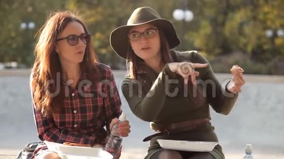 两个漂亮的女孩坐在公园里吃三明治喝水交流食物休息视频的预览图