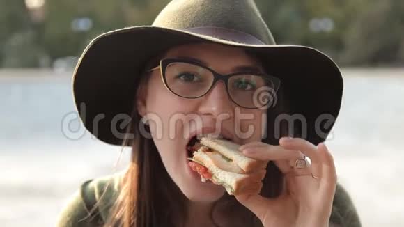 一个戴着眼镜和帽子的年轻女孩正在尝试一个美味的三明治食物视频的预览图