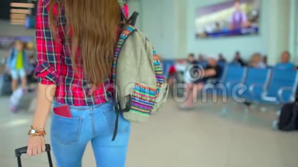 年轻的旅行女性穿着休闲衬衫带着行李在现代机场航站楼里行走特写镜头从后面看视频的预览图
