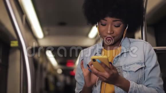 非洲裔美国年轻女性戴着耳机听音乐和在公共场合浏览手机的肖像视频的预览图