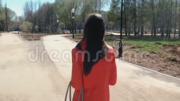 穿红色外套的年轻女子在春天公园散步后景视频的预览图