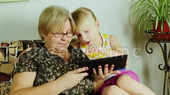 一位年迈的妇女和孙女一起在平板电脑上玩耍世代共用视频的预览图