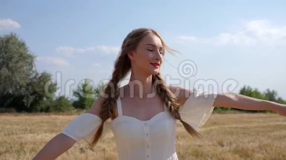 在阳光明媚的日子里快乐的女孩变成了一件白色的连衣裙辫子在田野里转动视频的预览图