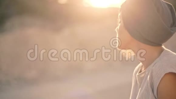 一位体贴而悲伤的女人坐在一条沙路和夕阳下的石头的背景上视频的预览图