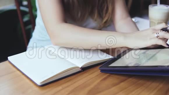 年轻美丽的欧洲女孩在炎热的夏日在咖啡馆里使用平板电脑提供冷牛奶和咖啡鸡尾酒关门视频的预览图