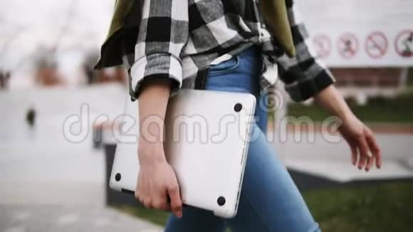 一个穿牛仔裤的优雅女孩手里拿着笔记本电脑穿过公园自信的散步侧视没有视频的预览图