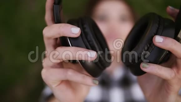 女性手中的耳机可爱的女孩躺在草地上戴上耳机听着视频的预览图