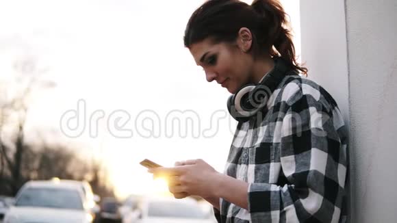 漂亮的女人站在白色的柱子附近手里拿着手机打字耳机太阳照耀着视频的预览图