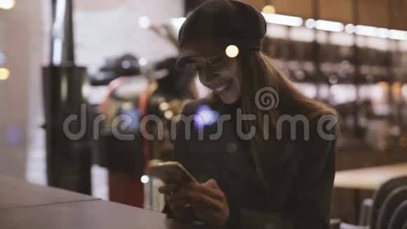 年轻漂亮时髦的黑发女人晚上坐在靠近窗户的咖啡屋里用电话视频的预览图