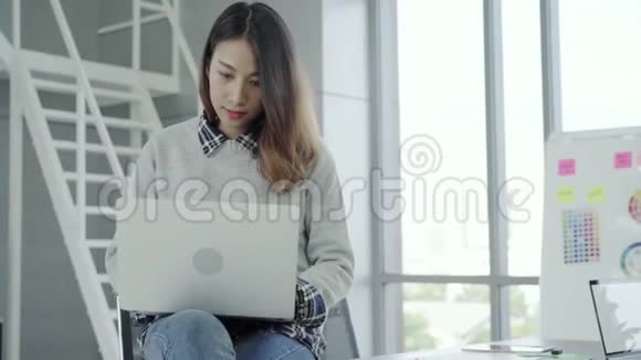 年轻的亚洲女经理在现代工作场所坐着时使用便携式电脑设备视频的预览图