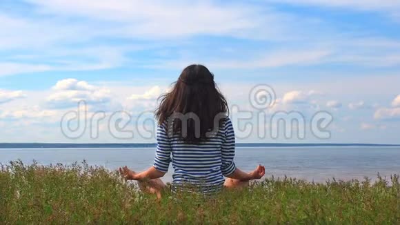 从后景看年轻女子穿着条纹衣服坐在河滩上的莲花姿态高加索女人的感觉视频的预览图