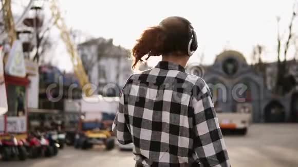 追踪拍摄一个年轻的棕色头发的女孩在阳光明媚的日子里带着耳机走在街上跳舞和视频的预览图